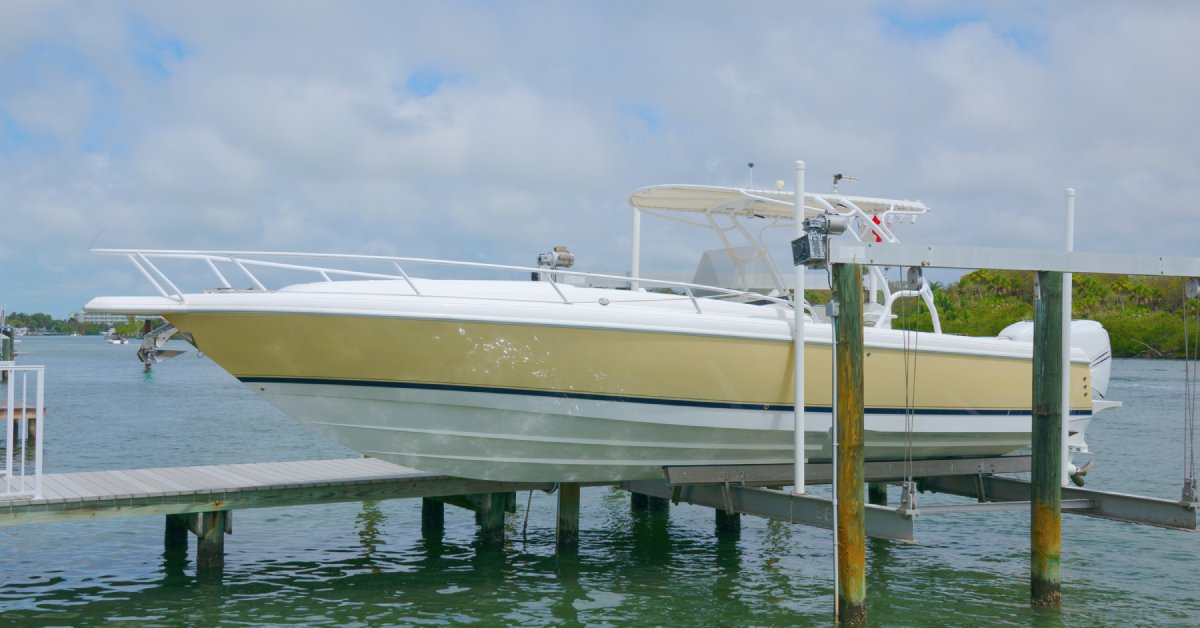 A speedboat with yellow and white paint is elevated on a vertical boat lift next to a marine dock.