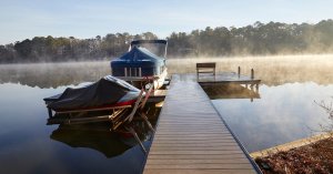 A lake boat dock in the morning with steam rising from the water. A covered PWC and pontoon are docked next to the structure.