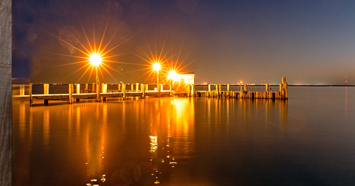 A pier at night with no visitors or boats nearby. Three bright orange lights are installed along the pier.
