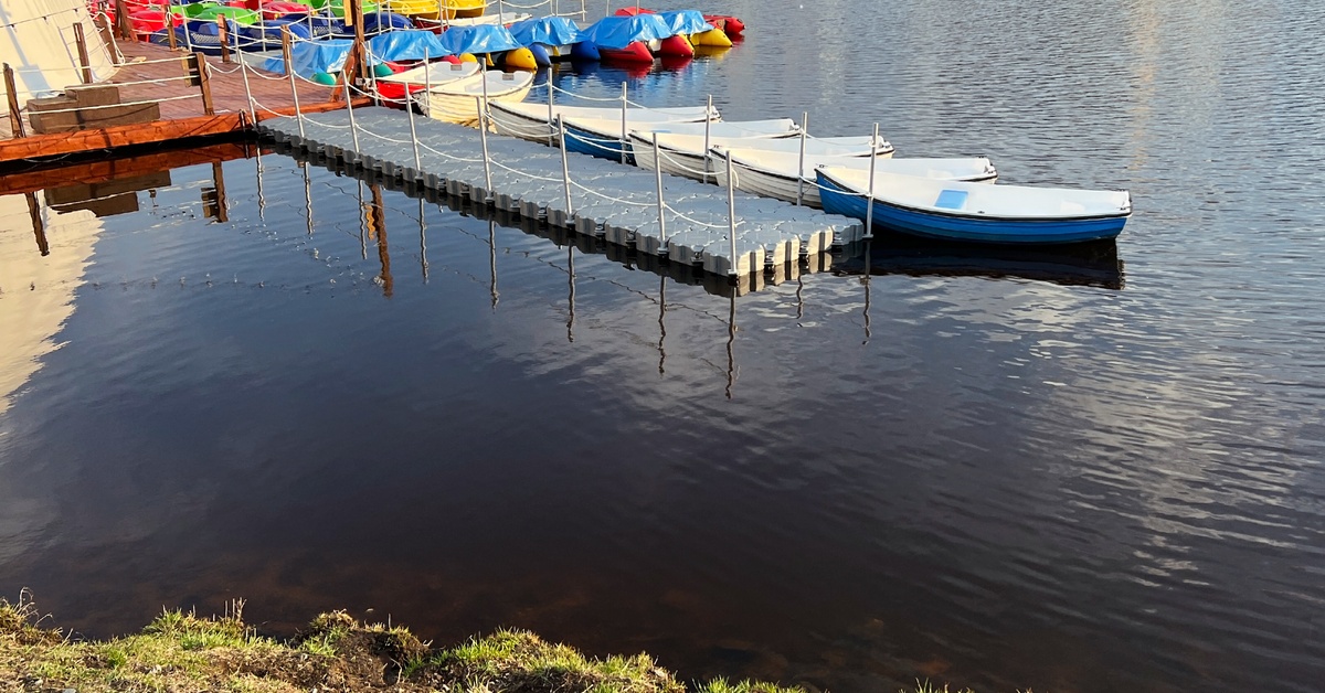A wooden pier with a long, gray modular floating dock attached to it. Boats are parked along both areas.
