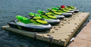 Six lime green water scooters parked on a large floating dock. One of them has a red fabric lying on it.