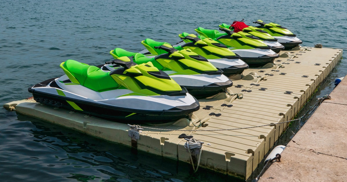 Six lime green water scooters parked on a large floating dock. One of them has a red fabric lying on it.