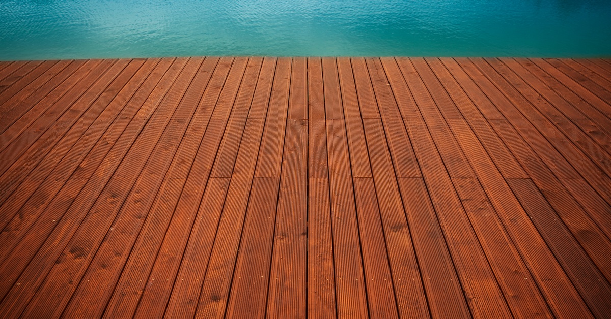 A wide stationary pier constructed of dark brown wooden planks. Blue water is visible at the edge of the pier.